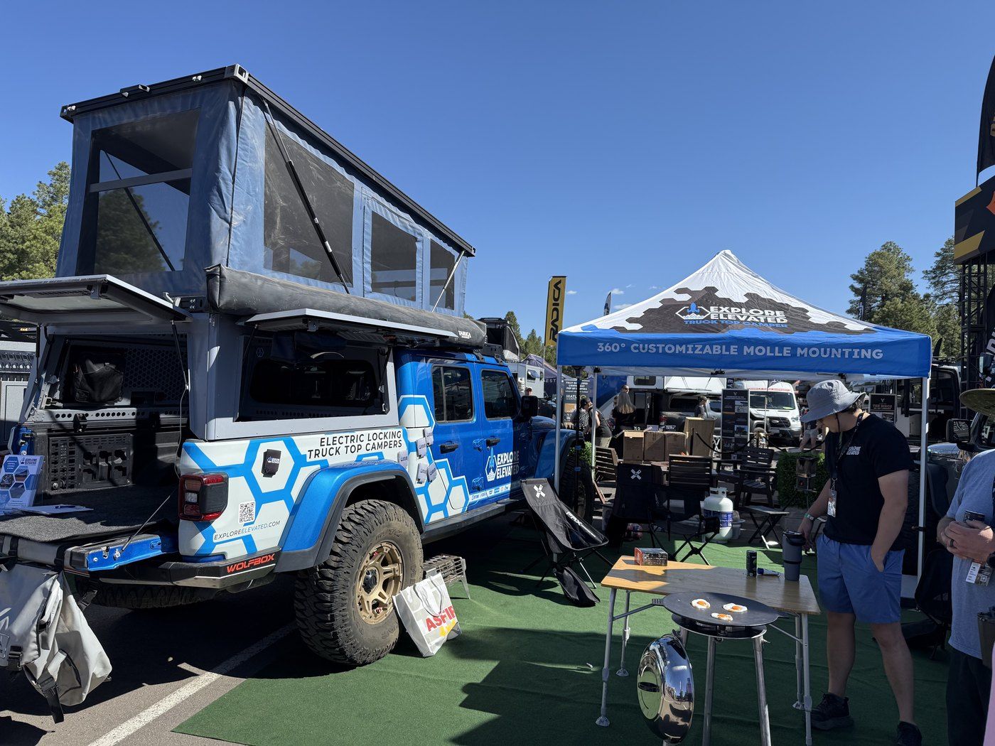 Explore Elevated truck-top camper and MOLLE mounting display at an overland show